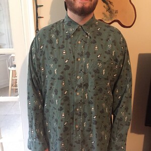 May include: A green long-sleeved button-down shirt with a pattern of various small images, including cars, clocks, and people.
