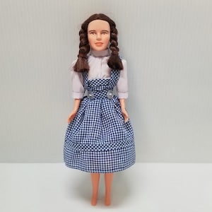 May include: A vintage doll with brown hair wearing a white blouse and a blue and white gingham dress.
