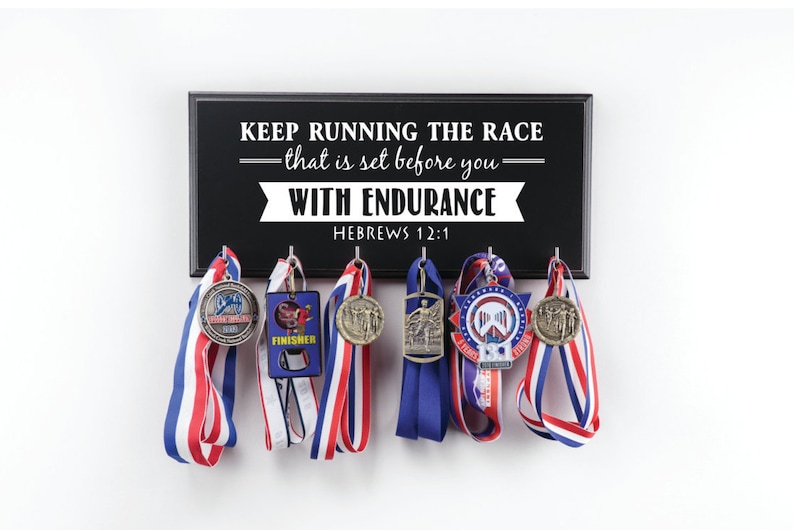 Puede incluir: Un soporte de madera negro para medallas con el texto "KEEP RUNNING THE RACE -that is set before you- WITH ENDURANCE HEBREWS 12:1" y varias medallas colgadas.