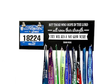May include: Black medal display rack with the quote "But those who hope in the Lord = will renew their strength = They will run & not grow weary Isaiah 40:31". The rack has hooks for hanging medals and a space for a race bib.