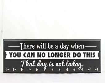 May include: Black rectangular wall decor with the text "There will be a day when YOU CAN NO LONGER DO THIS. That day is not today." The sign has small hooks along the bottom.