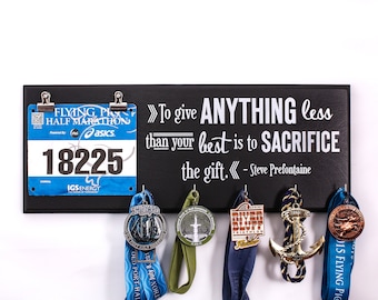 May include: Black chalkboard with the quote "To give ANYTHING less than your best is to SACRIFICE the gift. - Steve Prefontaine" and a runner's bib with the number 18225.  The board has hooks for hanging medals, and there are several medals hanging from the hooks.