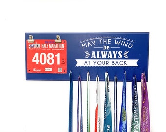 May include: A blue wooden sign with the text "May the wind be always at your back" and a hook for hanging medals. The sign has a red race bib with the number "4081s" attached to it.