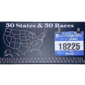 May include: A black board with a white outline of the United States map and the text "50 States & 50 Races". A blue running race bib with the text "Flying Pig Half Marathon" and the number "18225" is attached to the board with two silver clips.