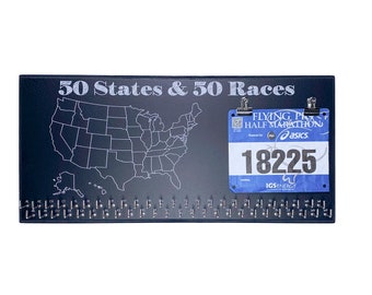 May include: A black board with a white outline of the United States map and the text "50 States & 50 Races". A blue running race bib with the text "Flying Pig Half Marathon" and the number "18225" is attached to the board with two silver clips.