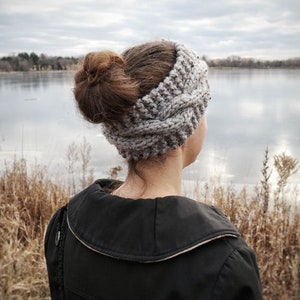 Pu&ograve; includere: Una fascia grigia lavorata a maglia con un motivo a trecce. La fascia &egrave; indossata da una persona con i capelli raccolti in uno chignon. La persona indossa una giacca nera e guarda un lago. La parola "ORNUTE" &egrave; stampata in basso.