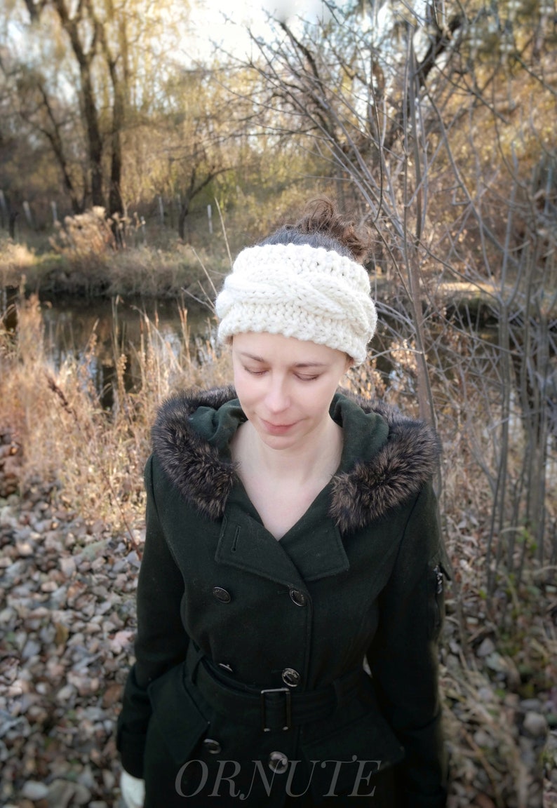 Pu&ograve; includere: Una fascia per capelli a trecce color crema. La fascia &egrave; spessa e sembra essere lavorata a mano. La persona indossa un cappotto verde scuro con cappuccio bordato di pelliccia. La parola "ORNUTE" &egrave; visibile in basso nell'immagine.