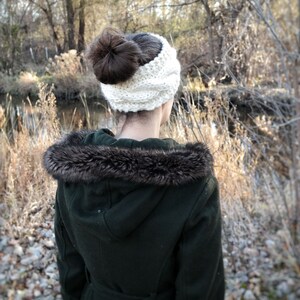 Pu&ograve; includere: Una donna indossa una fascia in maglia bianca con uno chignon marrone scuro. Indossa un cappotto verde scuro con cappuccio foderato in ecopelliccia. L'immagine &egrave; scattata all'aperto con uno sfondo naturale di alberi e un ruscello.