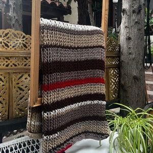 May include: A striped crocheted throw blanket with brown, beige, white, and red stripes hanging on a wooden frame.