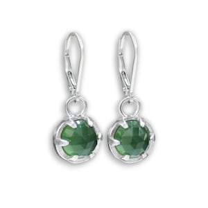 May include: A pair of silver dangle earrings with green gemstone accents. The earrings feature a round, faceted gemstone set in a silver bezel.