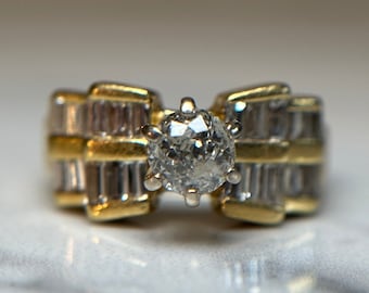 May include: A gold and silver ring with a large, round, clear diamond in the center. The band is set with smaller diamonds in a baguette shape.