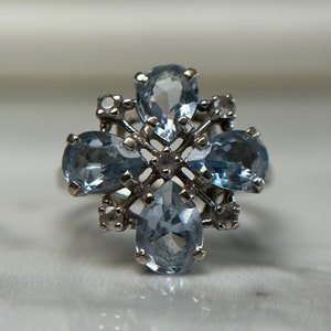 May include: A silver ring featuring a cluster of blue pear-shaped gemstones set in a delicate, intricate design.