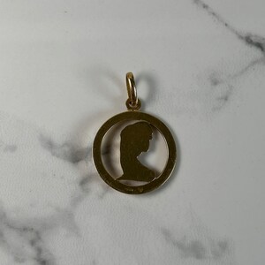 May include: Gold pendant with a cutout silhouette of a woman's head in profile.