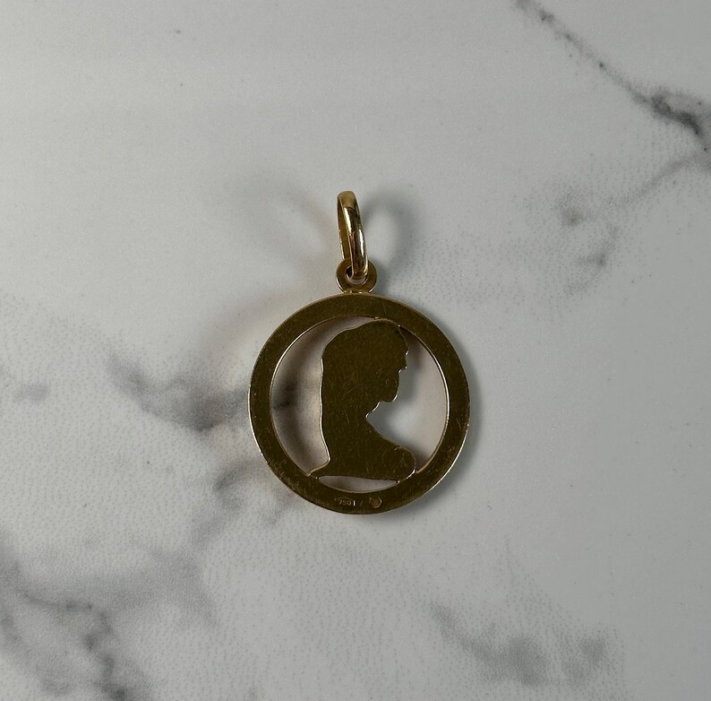 May include: Gold pendant with a cutout silhouette of a woman's head in profile.