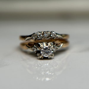 May include: A gold wedding band set with a single round diamond in the center and smaller diamonds on the band.