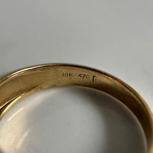 May include: Close-up of the inside of a gold ring with the inscription "10K, 420 F" on the band.