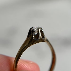 May include: A gold ring with a single, clear diamond set in a prong setting.