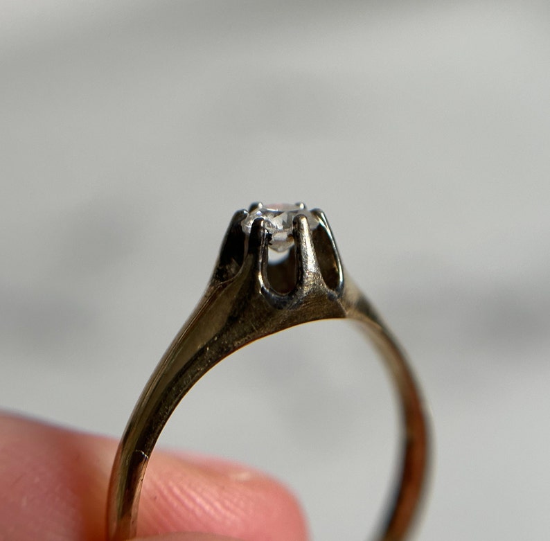 May include: A gold ring with a single, clear diamond set in a prong setting.