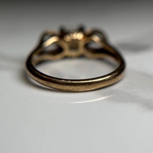 Puede incluir: Un anillo de oro con engaste de tres piedras. El anillo se muestra desde abajo, mostrando la banda lisa y redondeada.