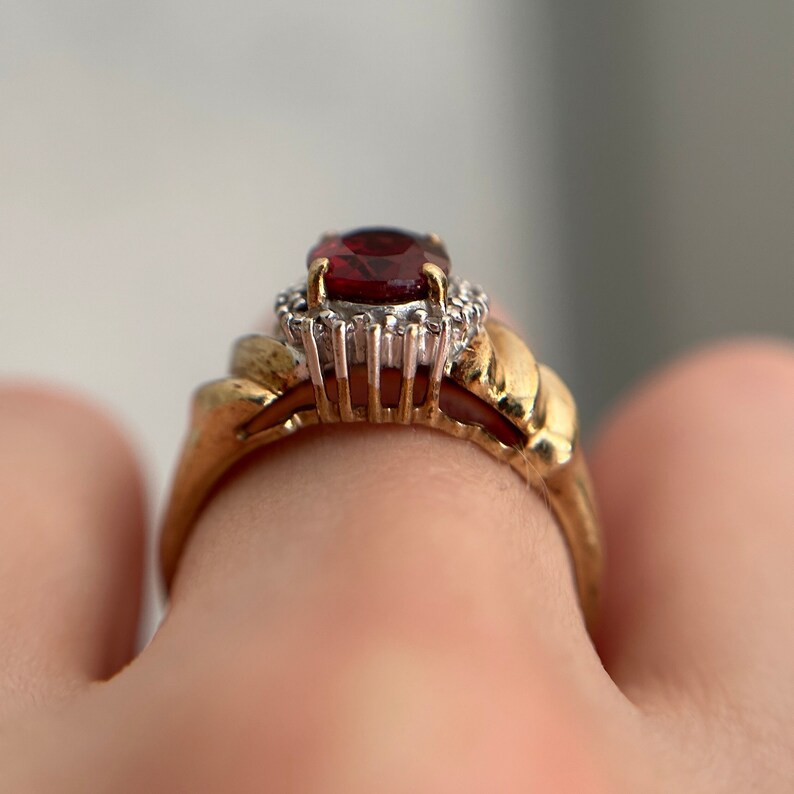 May include: A gold ring featuring a red gemstone surrounded by smaller white gemstones.