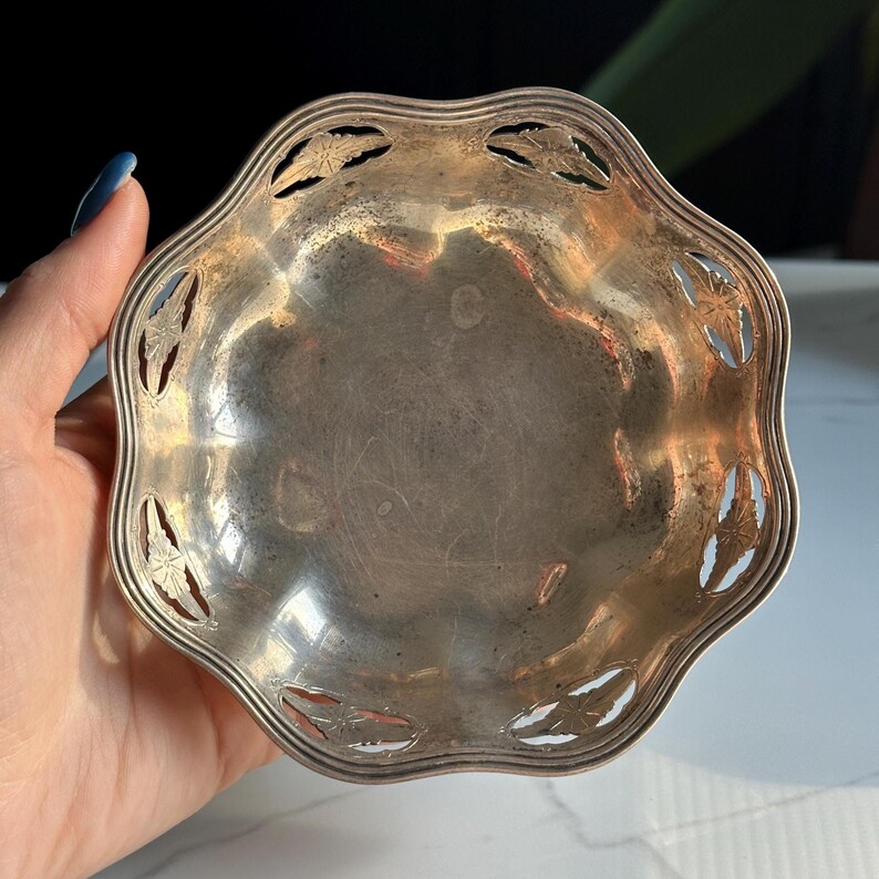 May include: A silver, scalloped, decorative dish with a cut-out design around the edge. The dish is slightly tarnished.