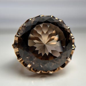May include: A gold ring featuring a large, faceted, smoky quartz gemstone. The gemstone is cut in a round shape and has a starburst pattern.