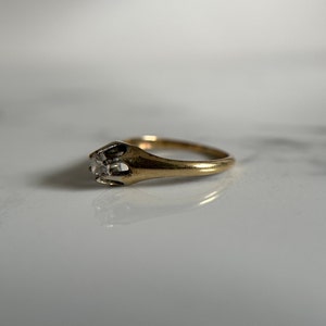 May include: A gold ring with a single, clear, square-shaped gemstone set in a prong setting.