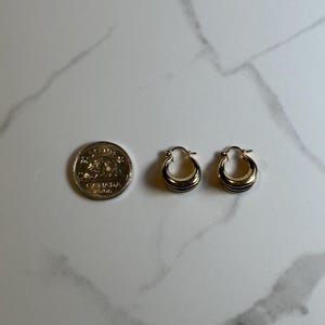 May include: A pair of gold hoop earrings with a slightly curved design. The earrings are about the size of a Canadian dime.
