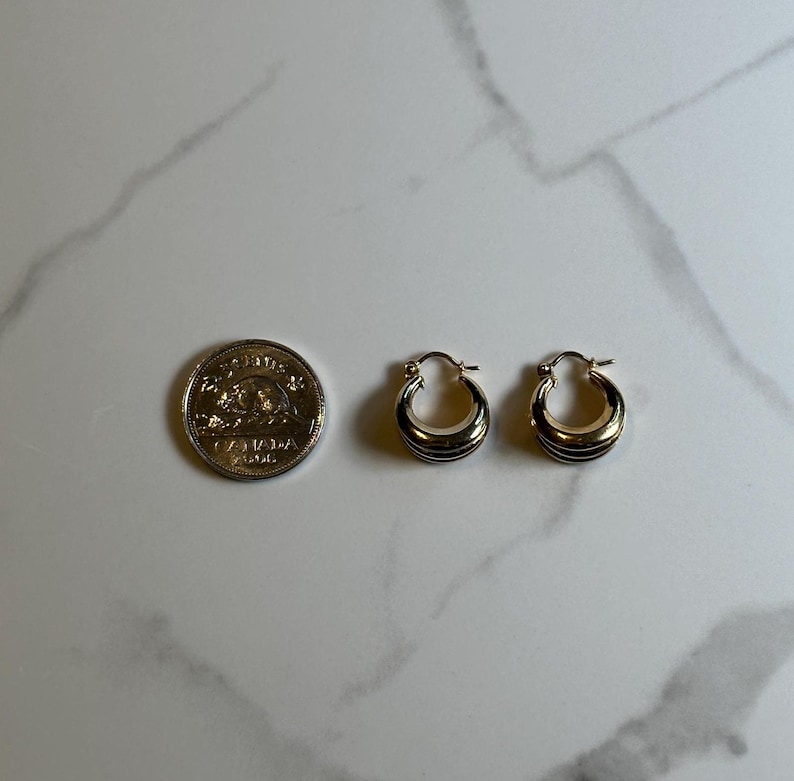 May include: A pair of gold hoop earrings with a slightly curved design. The earrings are about the size of a Canadian dime.