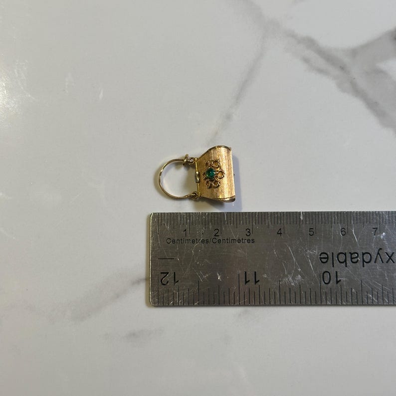 May include: A gold-colored earring with a textured surface and a small green gemstone in the center. The earring is approximately 1 inch in length and is next to a ruler.