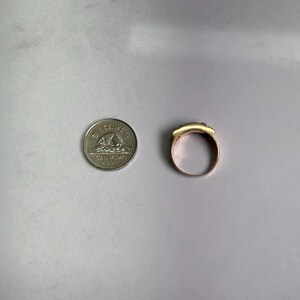 May include: A gold ring with a small gemstone setting is displayed next to a Canadian nickel coin. The ring has a simple band and a small, rectangular gemstone. The coin is silver in color and features a wildlife scene.