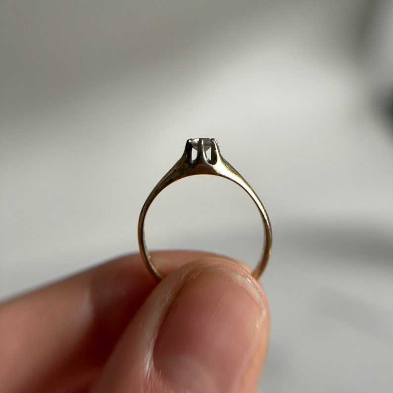 May include: A simple gold band ring with a single, clear, round-cut diamond set in the center.