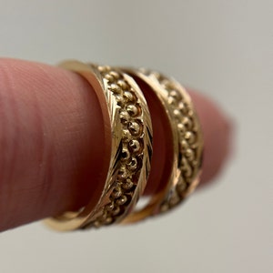 May include: Close-up of two gold rings. The rings have a textured design with small, raised beads and etched patterns. The rings are a warm gold color and appear to be made of metal. The rings are likely for a wedding or engagement.