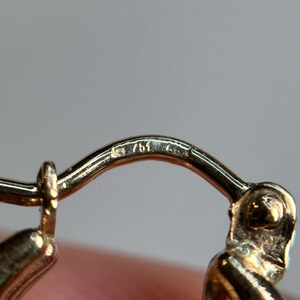 May include: Close-up of a gold earring with a hallmark of "750" on the back.
