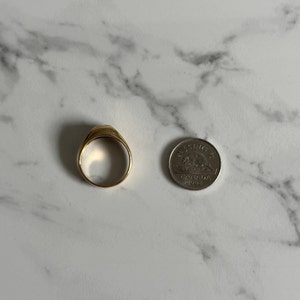 May include: A gold signet ring with a flat top, shown next to a Canadian 25-cent coin for size comparison.