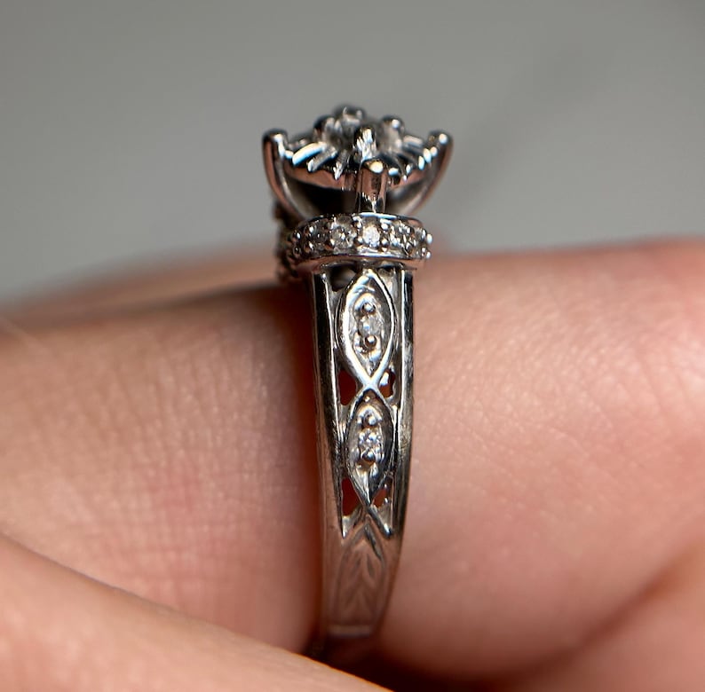 May include: A silver engagement ring with a diamond center stone and smaller diamonds set in the band. The band is intricately designed with a delicate floral pattern.