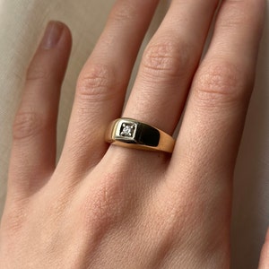 May include: A gold signet ring with a single, small, clear diamond set in the center.