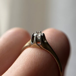 May include: A gold ring with a single, clear diamond set in a prong setting.