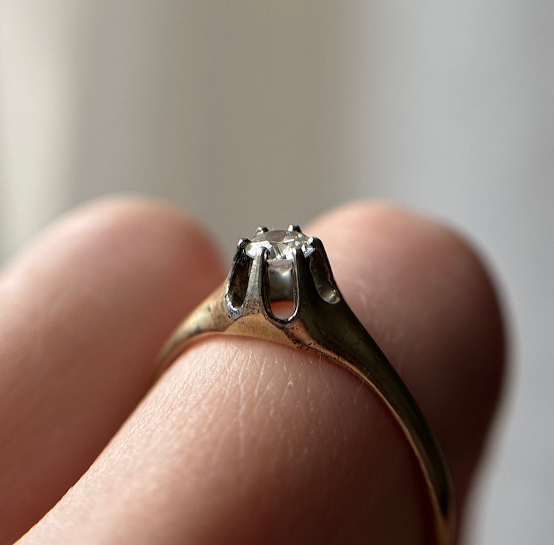May include: A gold ring with a single, clear diamond set in a prong setting.