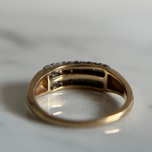 May include: A gold band ring with a row of small diamonds set in a channel setting. The ring has a simple, classic design.