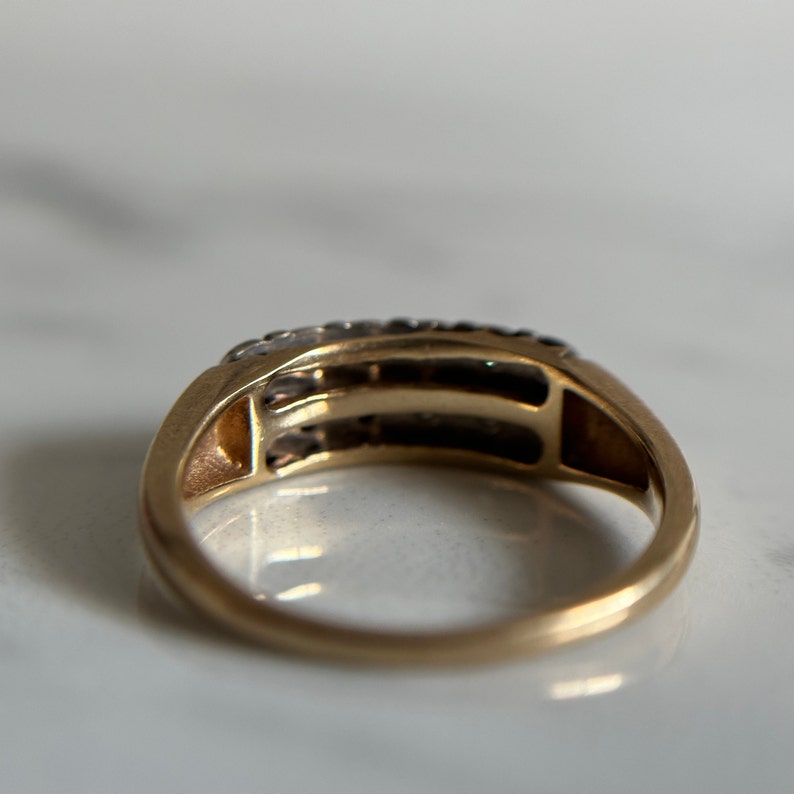 May include: A gold band ring with a row of small diamonds set in a channel setting. The ring has a simple, classic design.