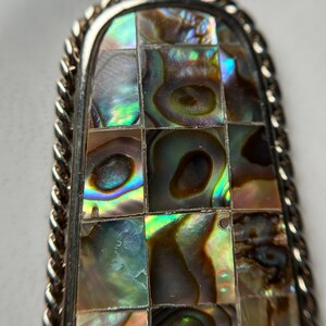 May include: A silver pendant with a rectangular abalone shell inlay. The shell is cut into small squares and arranged in a grid pattern. The shell has iridescent colors of green, blue, and brown.