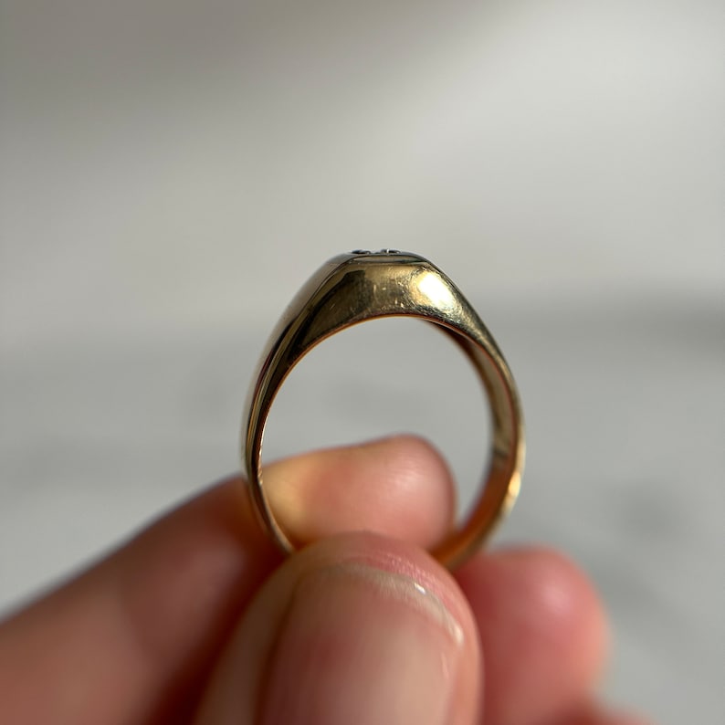 May include: A gold signet ring with a single small diamond set in the top. The ring is worn on a finger.