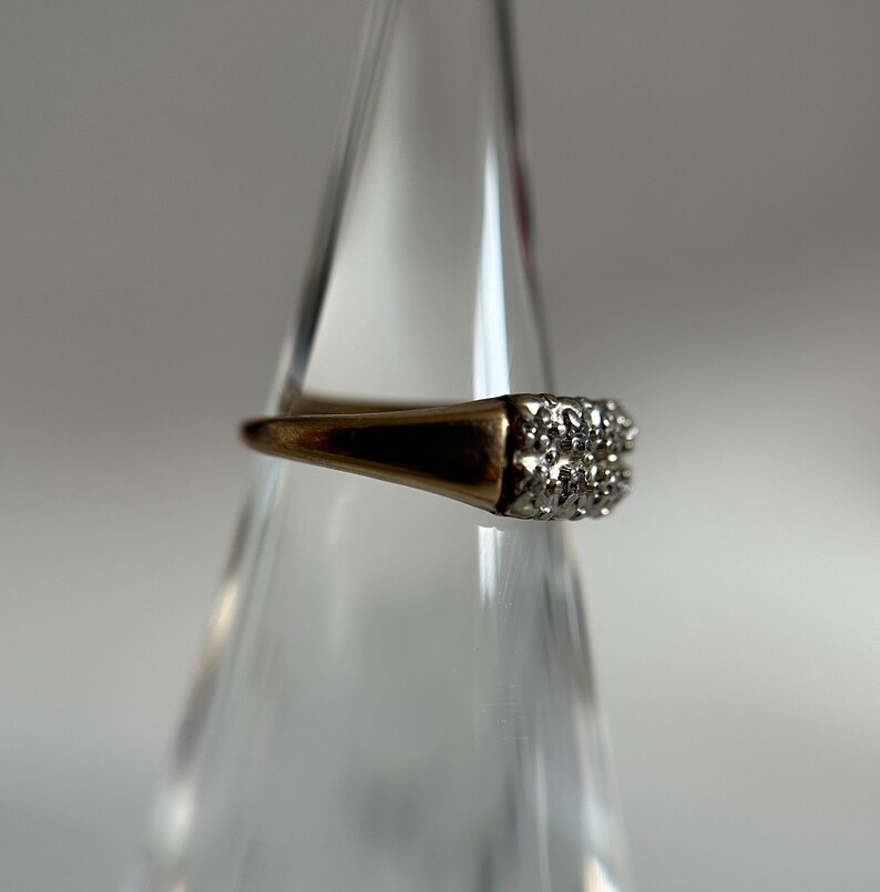 May include: A gold ring with a square-shaped setting of small, clear diamonds.