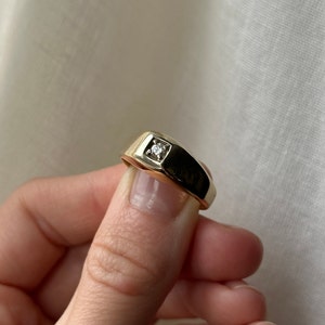 May include: A gold band ring with a single, small, clear diamond set in the center.