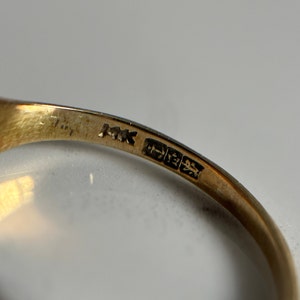 May include: Close-up of the inside of a gold ring with the inscription "MK" and a hallmark.
