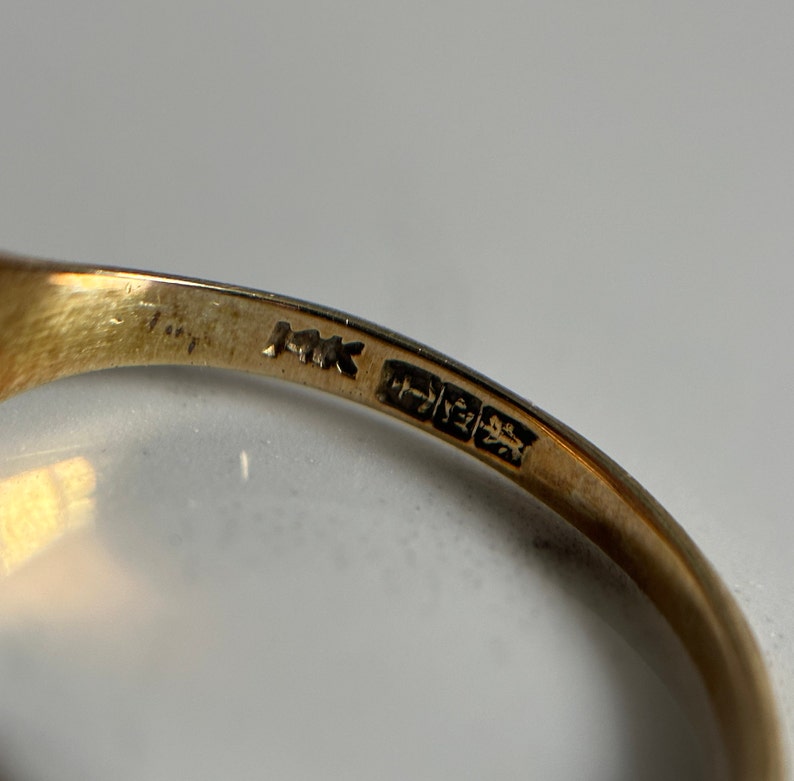 May include: Close-up of the inside of a gold ring with the inscription "MK" and a hallmark.