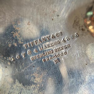May include: Close-up of a silver hallmark on a piece of silverware. The hallmark reads "Tiffany & Co. 167 8 4 Makers 483 Sterling Silver 925-1000  JM".
