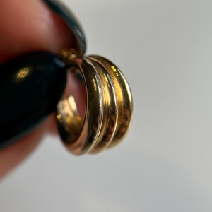 May include: Gold hoop earrings with three layers. The earrings are a classic style and would be a great addition to any jewelry collection.