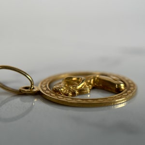 May include: A gold pendant with a detailed design of a woman's figure in a circle. The pendant has a loop for attaching to a chain.